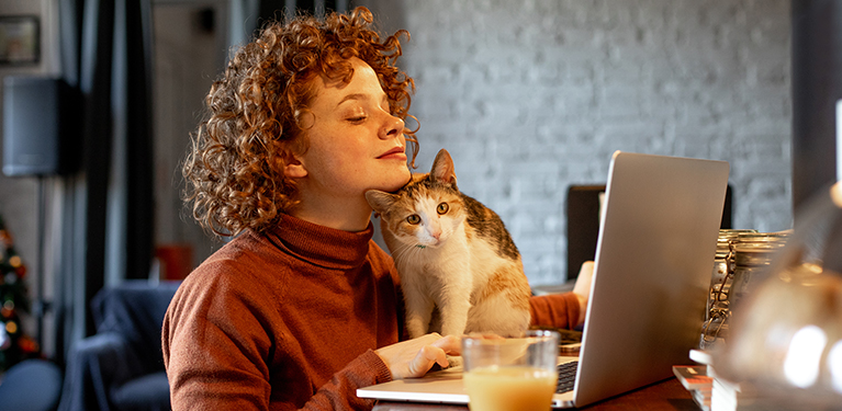 Photo of a person holding a cat in front of a computer 